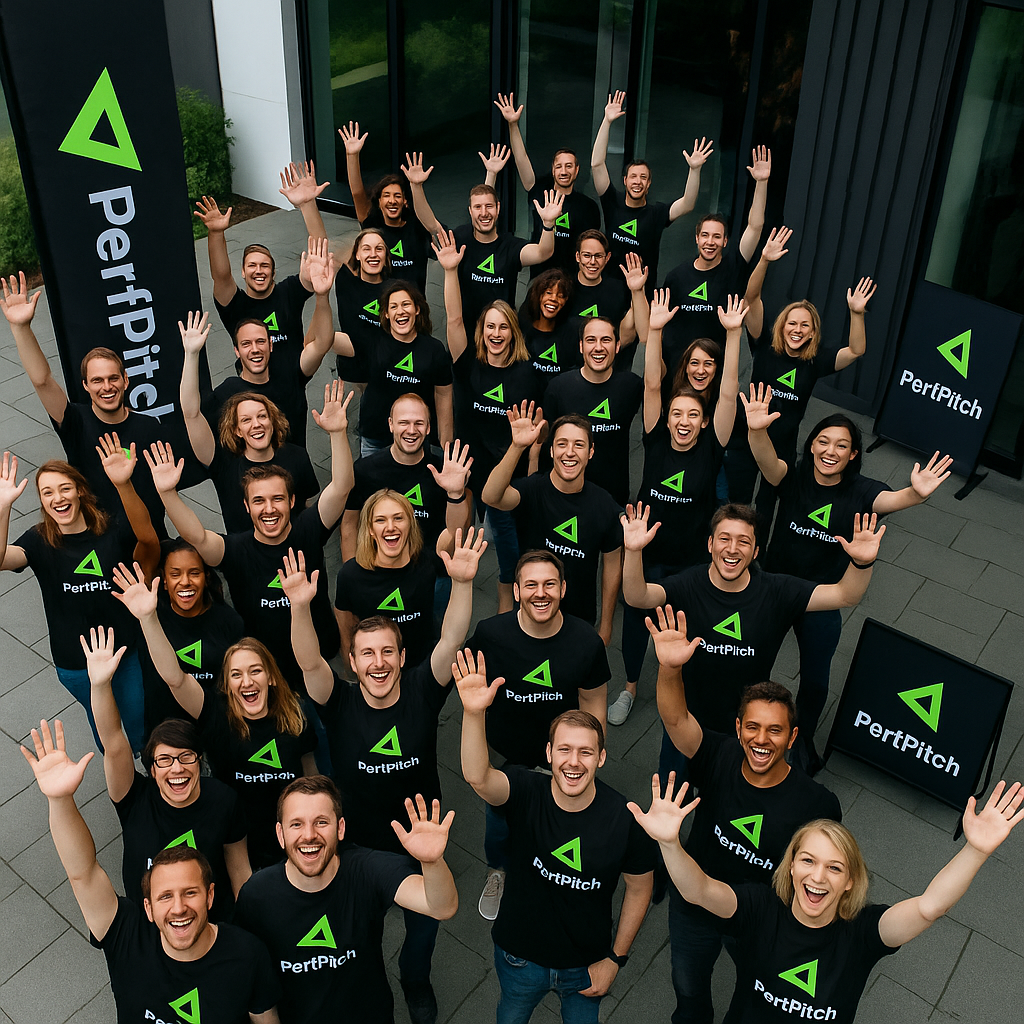 Crowd of 40 people in black PerfPitch t-shirts waving up at the drone in front of a building